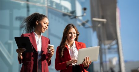 Two Asian businesswomen discussing business information while standing outside the office.